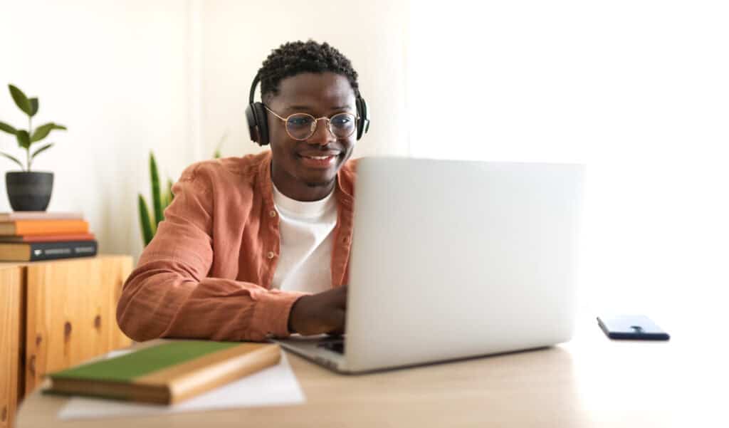 A college student sitting at a desk and doing work on his laptop.